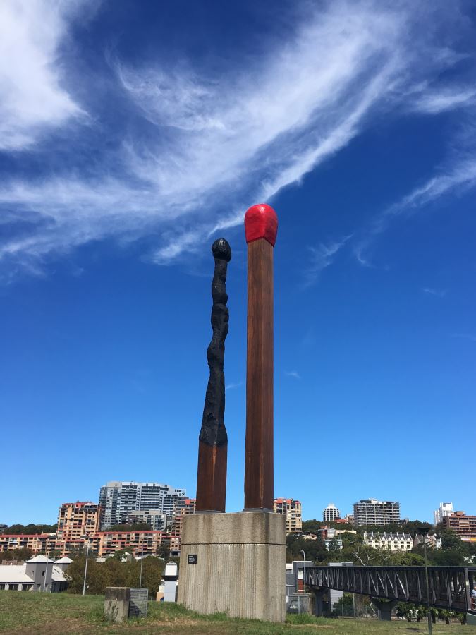 Two giant matchsticks, one burned, stand on a hillside in Sydney