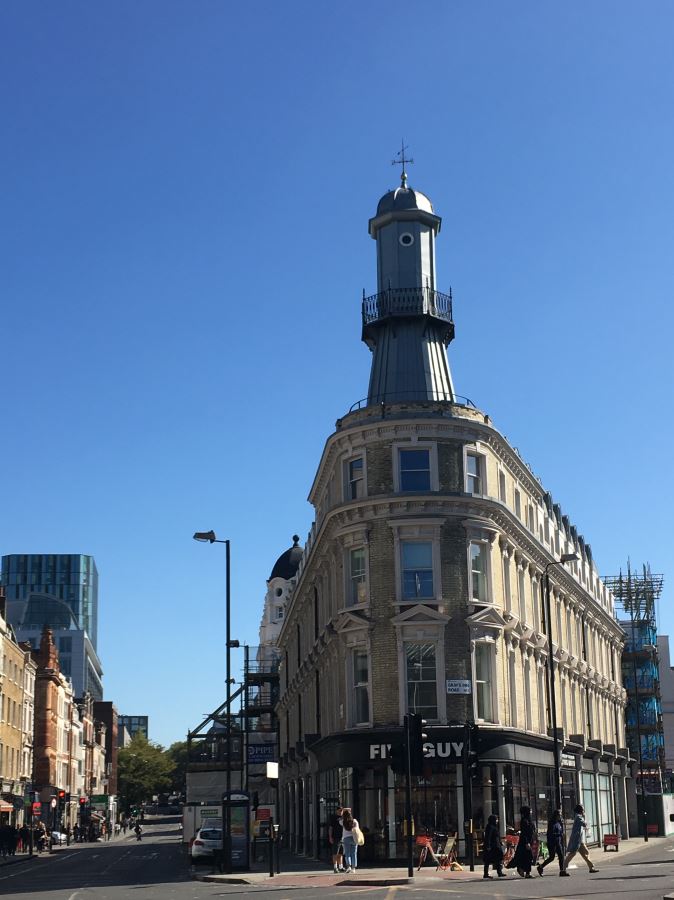A grey lighthouse like building sites on the roof of a normal building in Kings Cross London