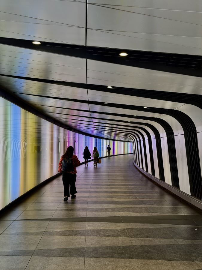 people walk down the lit up Rainbow Tunnel in Kings Cross London