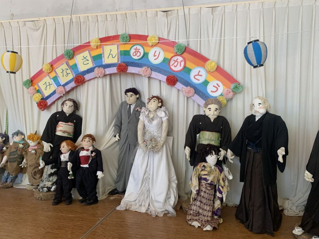 Scarecrows in the shape of a bridge and groom, plus a wedding party, some in Japanese dress, some in black tie at Scarecrow Village in Japan