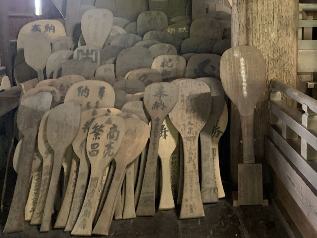 A pile of rice scoops carved from wood with writing on them sits against the wall in Senjojaku hall, Miyajima